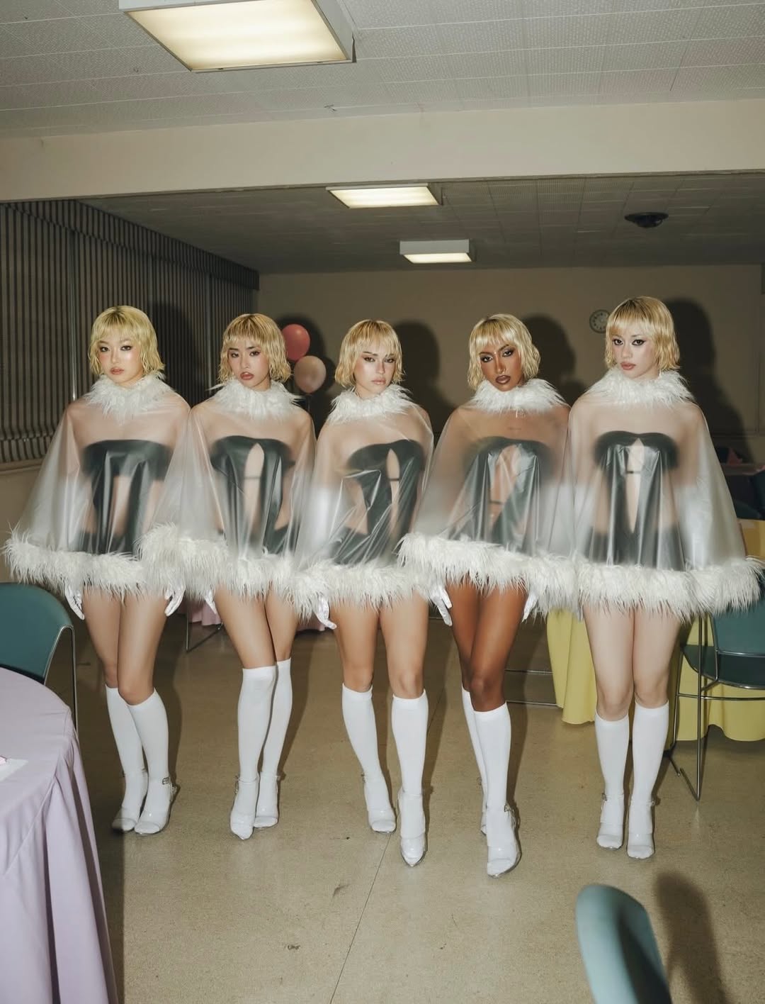 Girl group Katseye posed in a straight line with identical short blonde wigs and cropped dressed.
